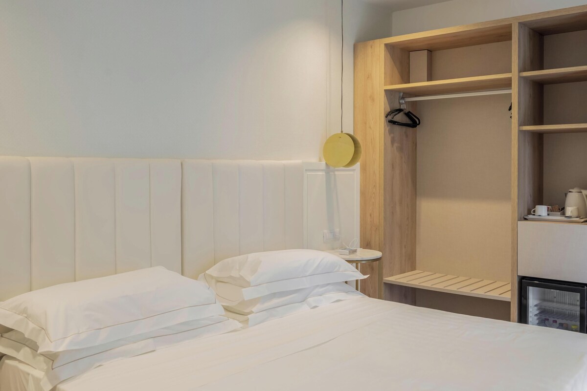 Une chambre d’hôtel avec un lit, une armoire en bois, une petite table avec une bouilloire et un luminaire suspendu.