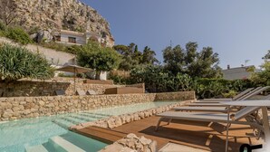 A pool area with stone steps, lounge chairs, and a view of a mountainous landscape. - Hotiday Mondello Beach (Palermo)