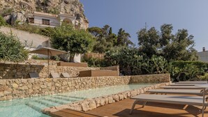 Un espace piscine agrémenté d’escaliers en pierre, de chaises longues et offrant une vue sur un paysage montagneux.