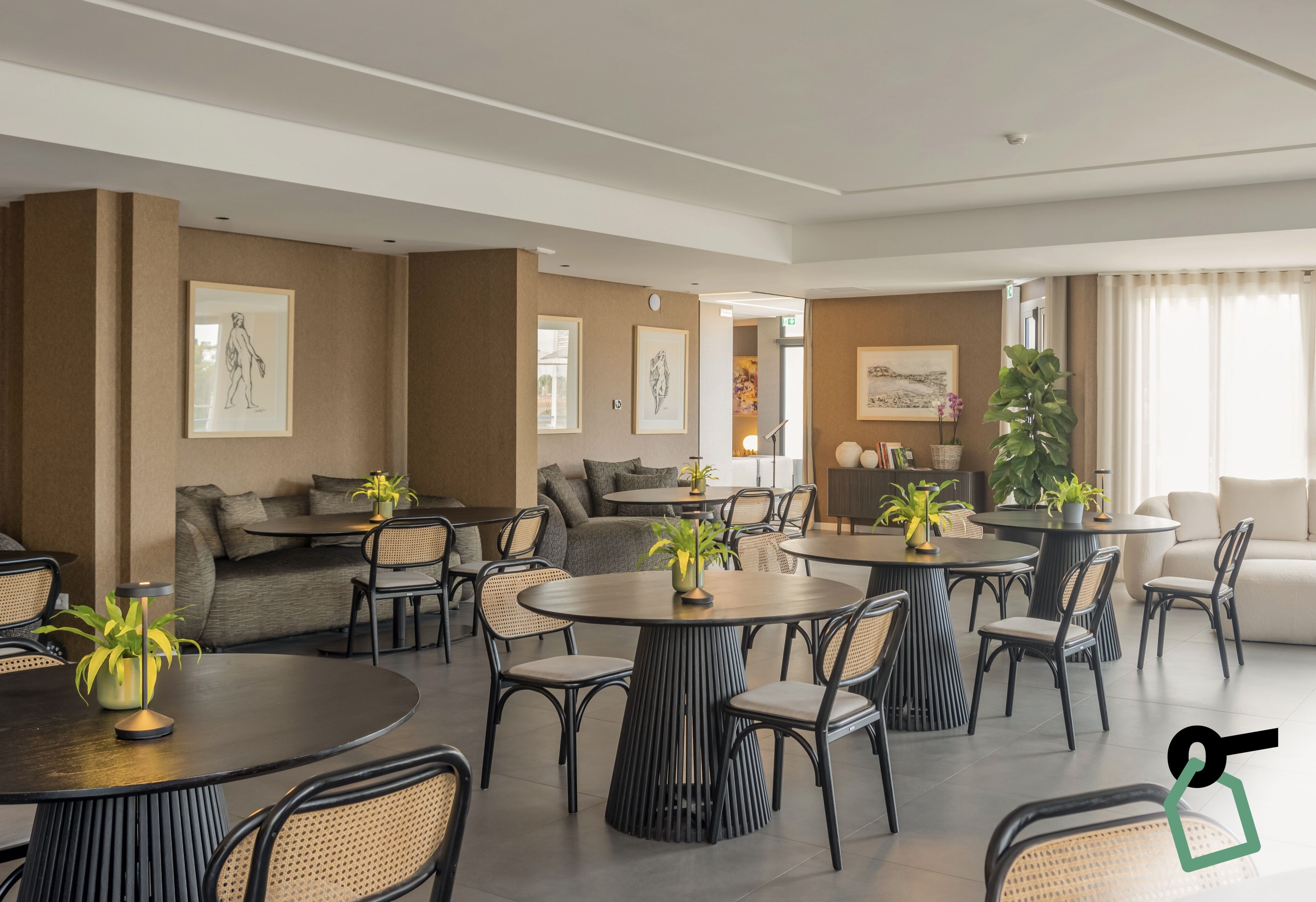 Eine moderne Hotelhalle mit runden Tischen, bequemen Sitzgelegenheiten und Kunstwerken an den Wänden.