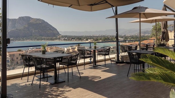 Une terrasse extérieure avec des tables et des chaises, des parasols et une vue sur la mer et les montagnes.