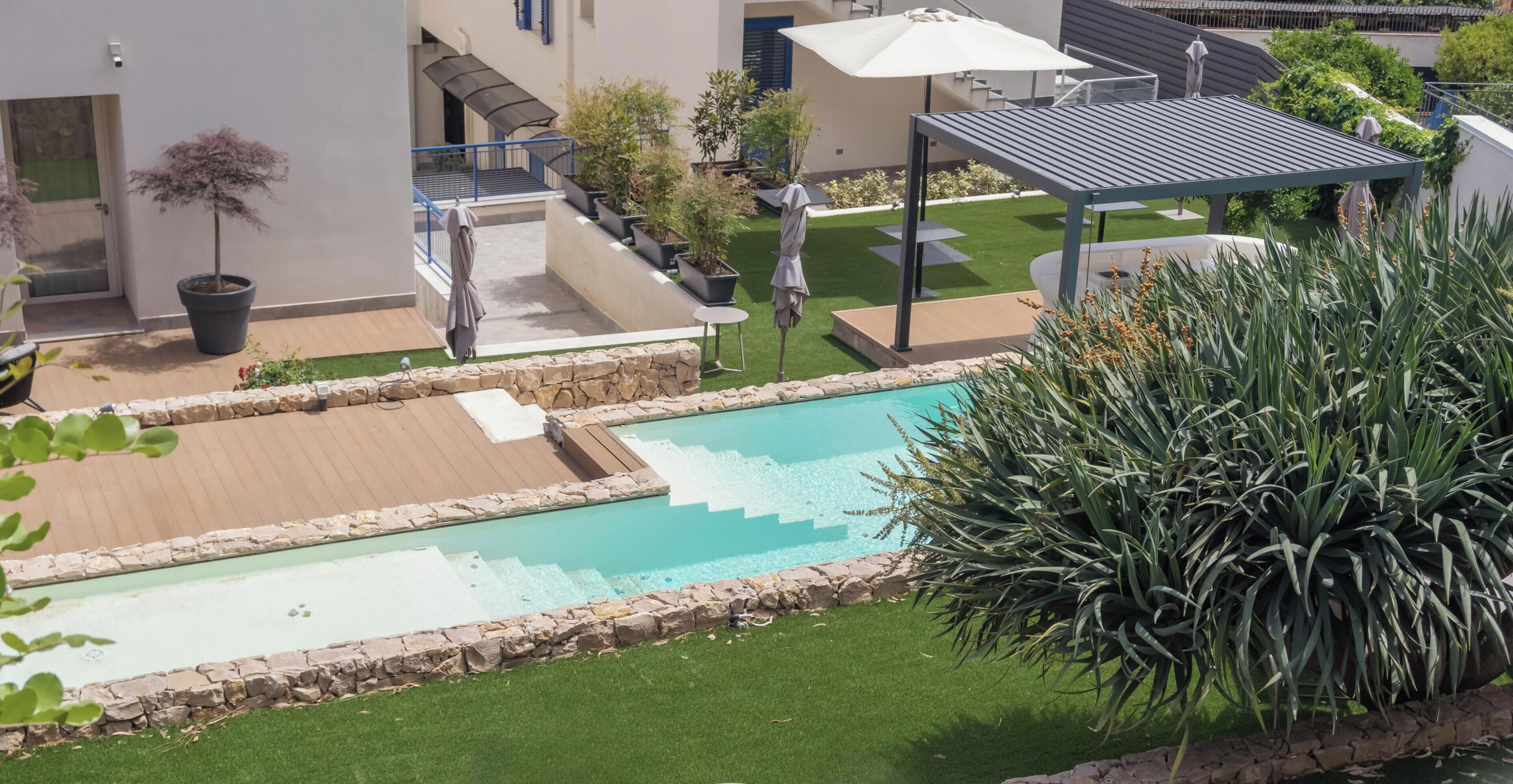A swimming pool with a stone border, a covered patio area, and a grassy lawn with potted plants.