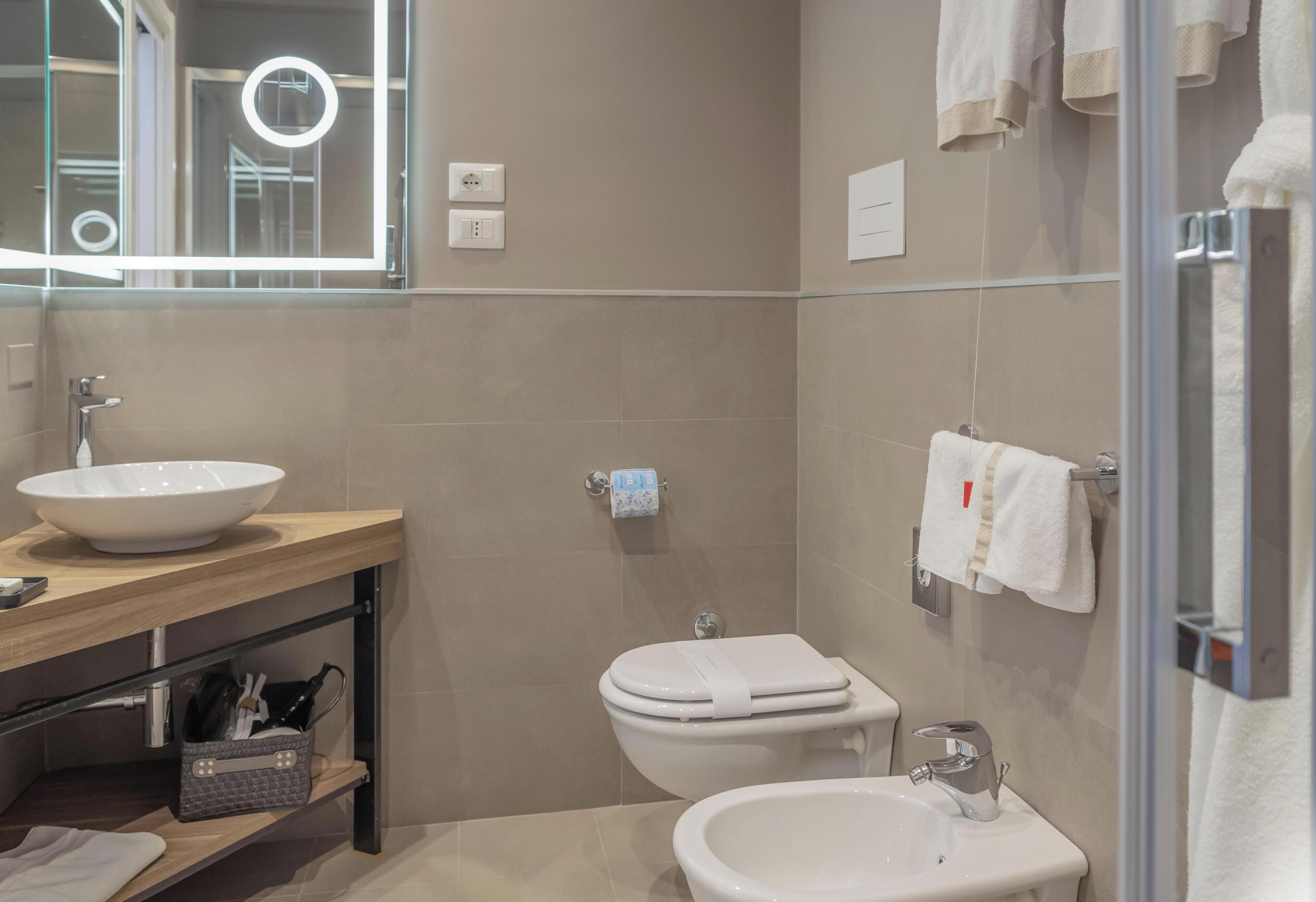 A modern bathroom with a large mirror, a sink, a toilet, and a bidet.