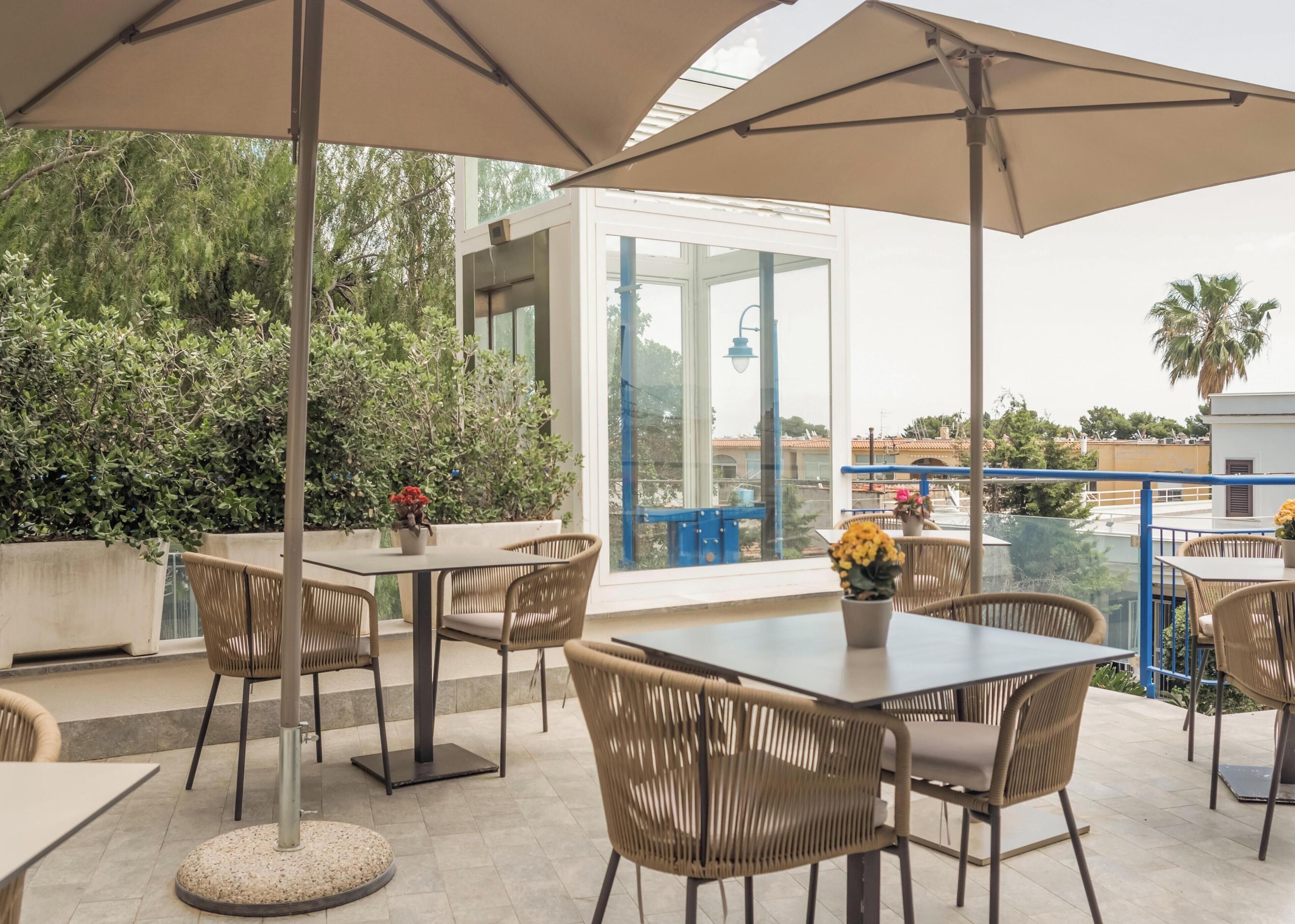 An outdoor patio with tables and chairs, a large umbrella, and potted plants.