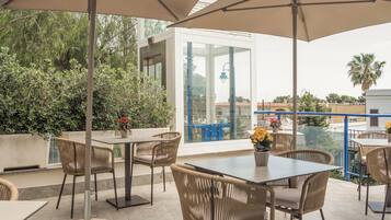 An outdoor patio with tables and chairs, a large umbrella, and potted plants.