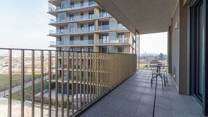 A balcony with a view of a multi-story building, a metal railing, and a small table with chairs. - Italianway Comfort - Pasolini 70 B - Feel Uptown (Milano)