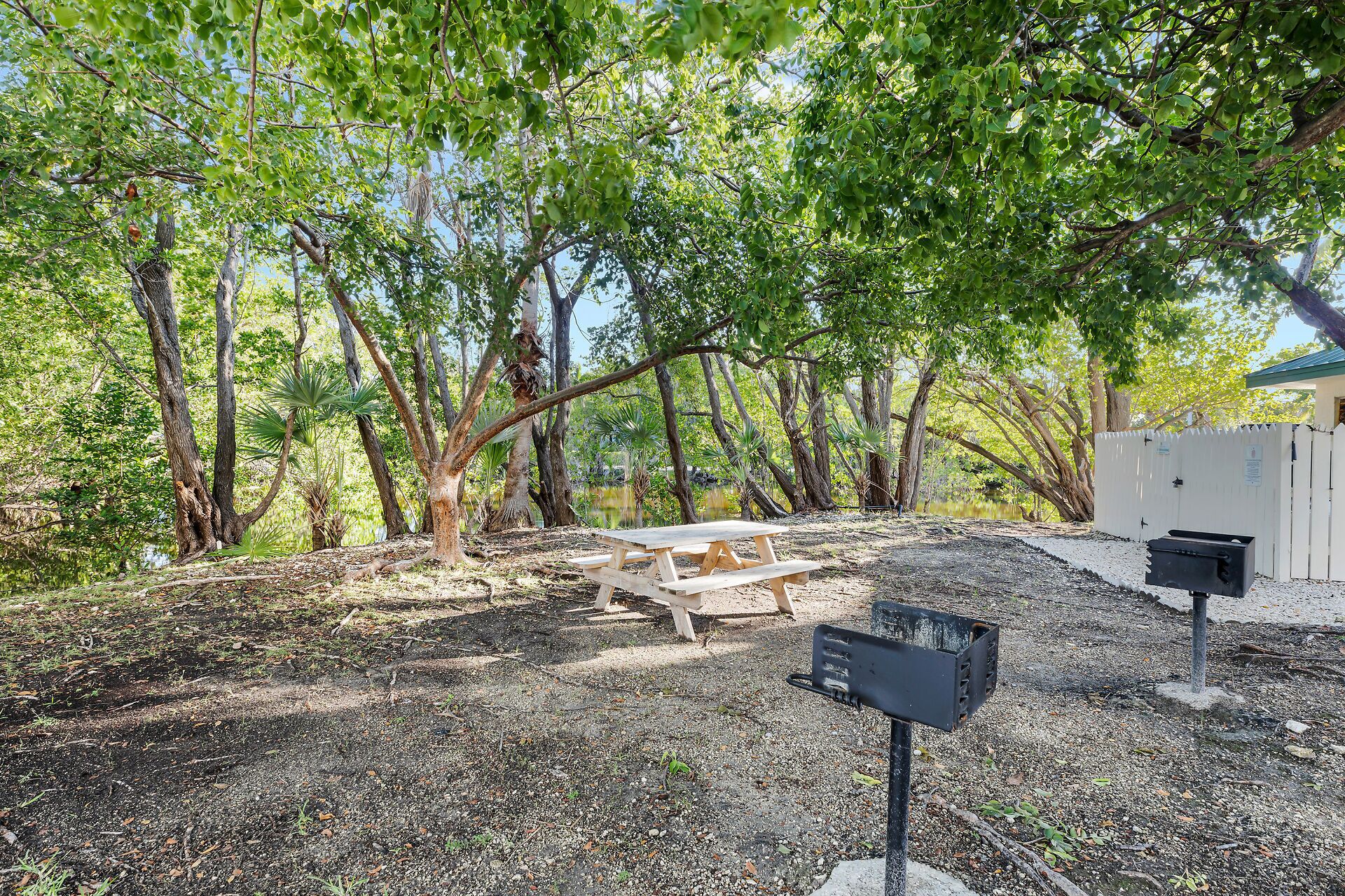 A picnic table in a wooded area with a white fence and a utility box.