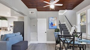 A modern living room with a gray sofa, a dining table with chairs, a ceiling fan, and a staircase leading to another level.