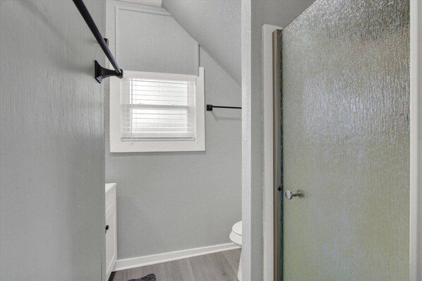 Un baño con ducha, inodoro y ventana con persianas.