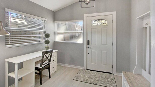 A room with a white desk, a chair, a door with a decorative glass panel, and a small rug on the floor.