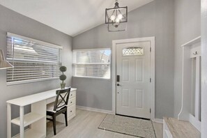 Una habitación con un escritorio blanco, una silla, una puerta con un panel de vidrio decorativo y una pequeña alfombra en el suelo.