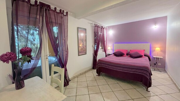 A bedroom with a bed, two bedside lamps, a nightstand, a chair, a table, and a vase with flowers. - Gîte des Orgues d'Ille Eucalyptus (Ille-sur-Têt)