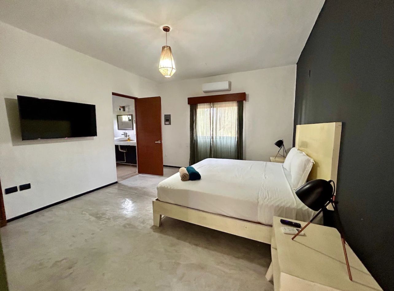 A bedroom with a bed, a TV, a bedside lamp, and a window with curtains.