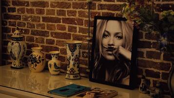 A brick wall, a framed portrait, and decorative vases on a shelf.