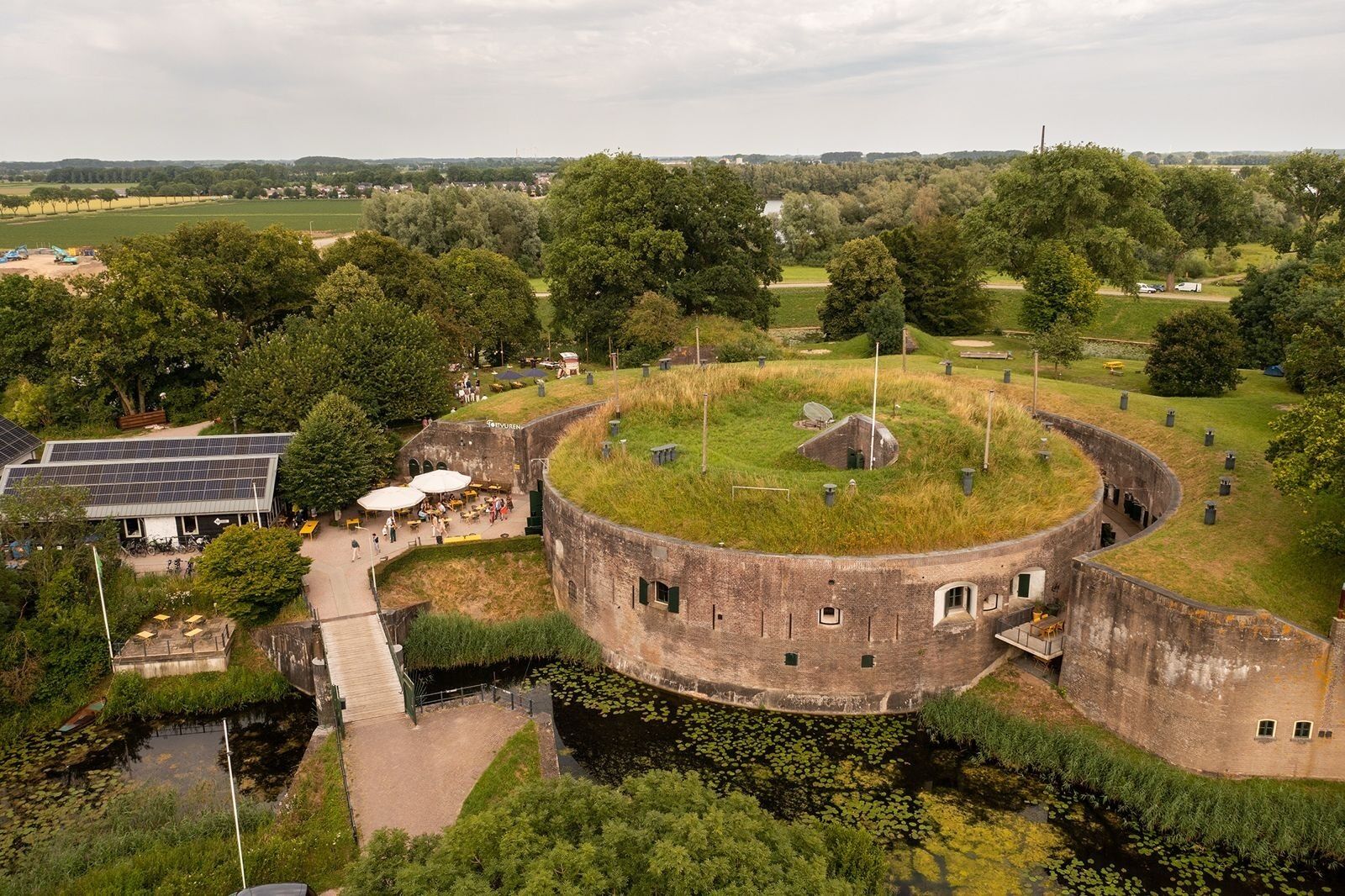 Un fort circulaire, surmonté d’une butte herbeuse, entouré d’arbres et bordé d’un petit étang.