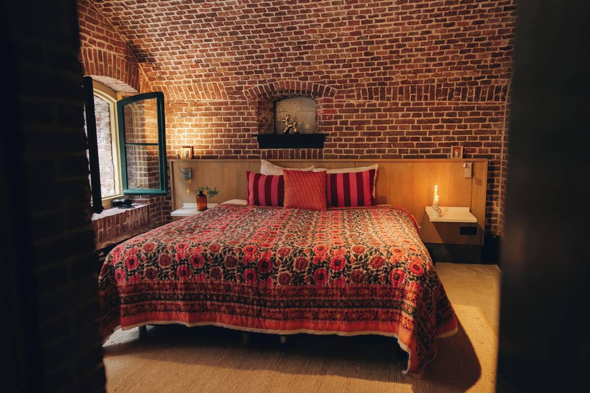 A bedroom with a brick-patterned ceiling, a bed with a floral-patterned bedspread, a wooden headboard, and a nightstand with a lamp.
