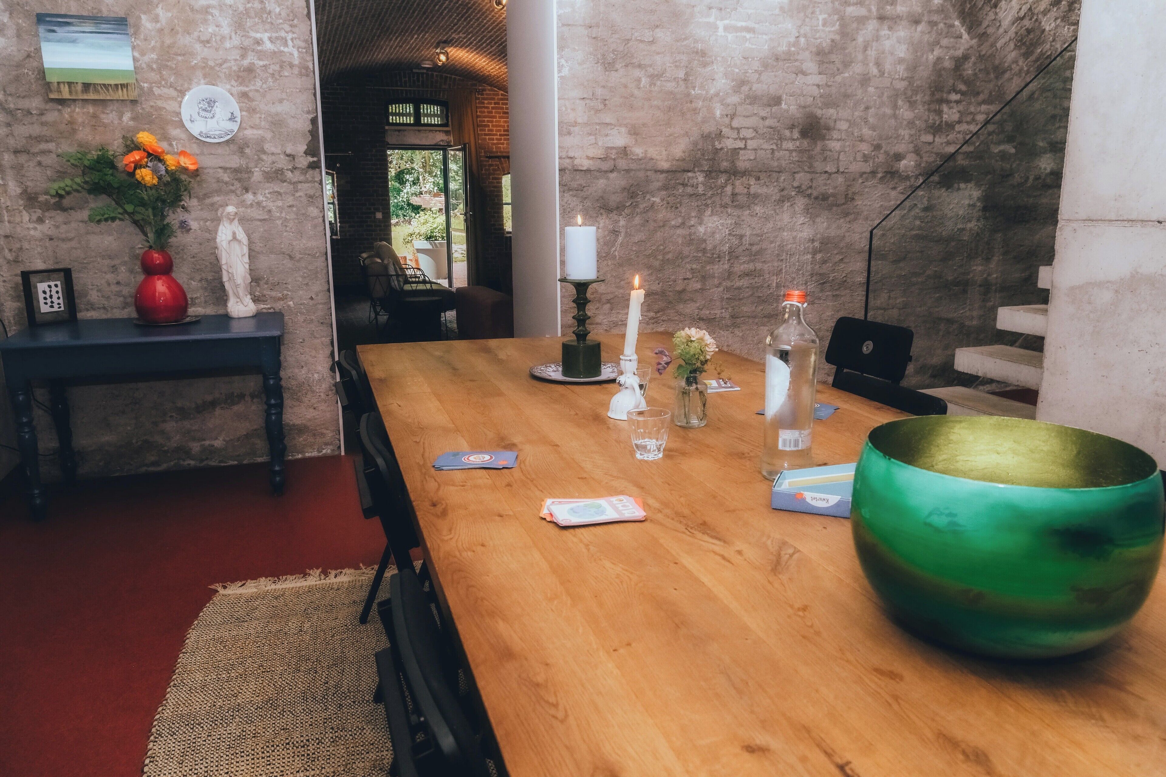 A wooden dining table with a green bowl, candles, and a vase with flowers.
