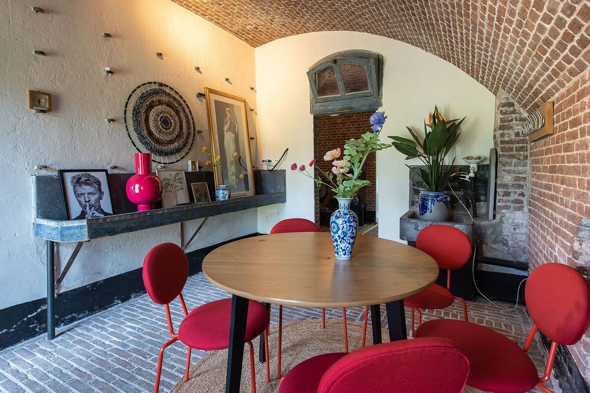 A cozy dining area with a brick wall, a round wooden table, and red chairs.