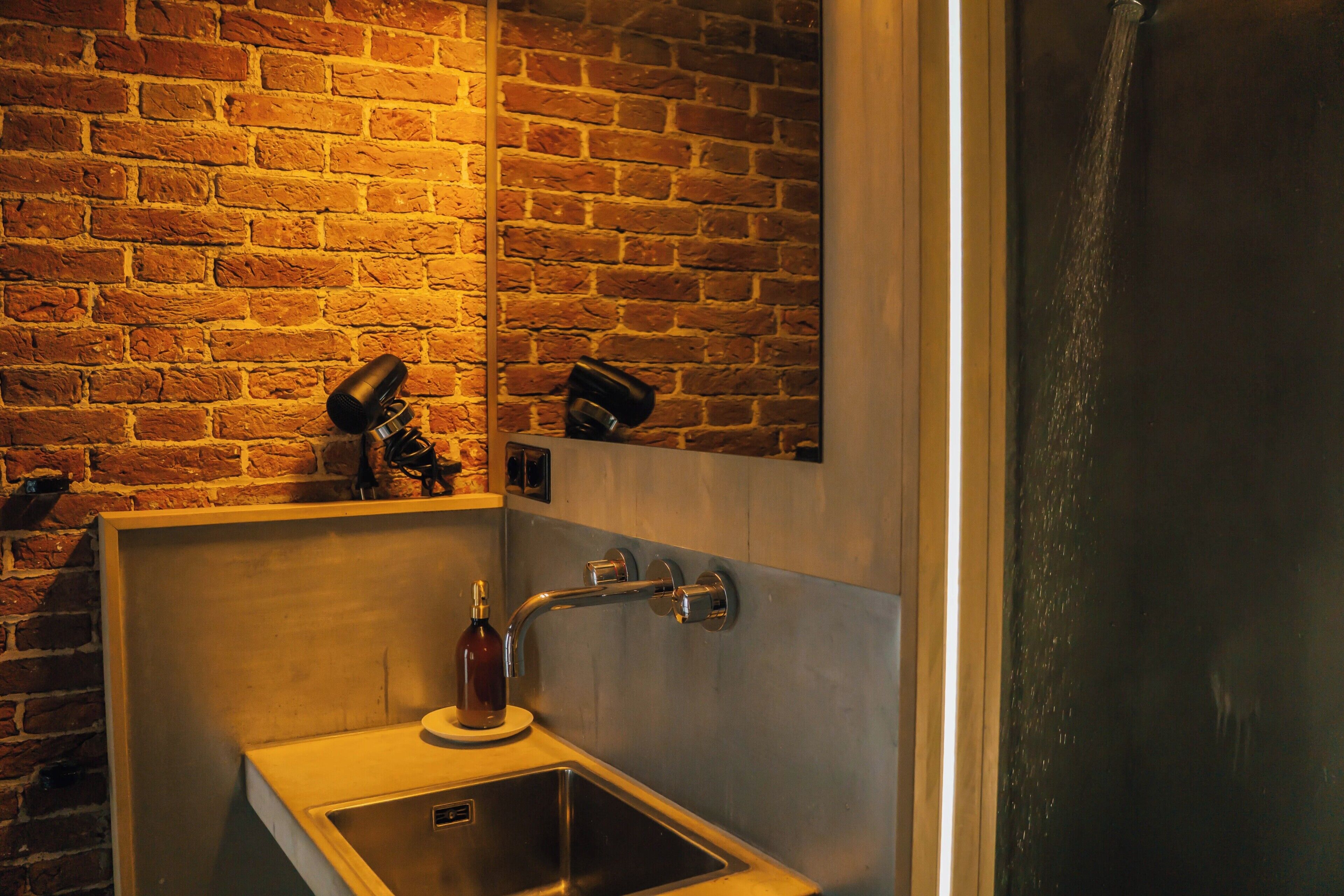 A bathroom with a brick wall, a sink, a mirror, and a shower.
