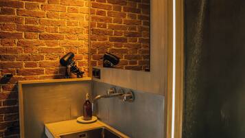 A bathroom with a brick wall, a sink, a mirror, and a shower.