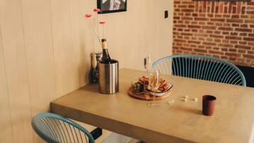 A dining area with a wooden table, two blue chairs, a bottle of champagne, a glass, and a plate of food.