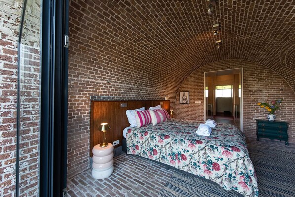 Ein Zimmer mit Ziegeldecke, einem Bett mit Blumenmuster-Bettwäsche, einer Nachttischlampe und einem Schminktisch mit Blumenvase.