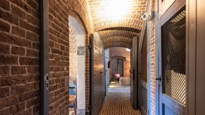 A brick-walled hallway with a tiled floor leading to a room with a wooden door and a mesh screen. - Fort Vuren (Vuren)