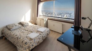 A bedroom with a bed, a desk, a chair, a window with a city view, and a hanging lamp. - Breathtaking view - Private garage (Rennes)