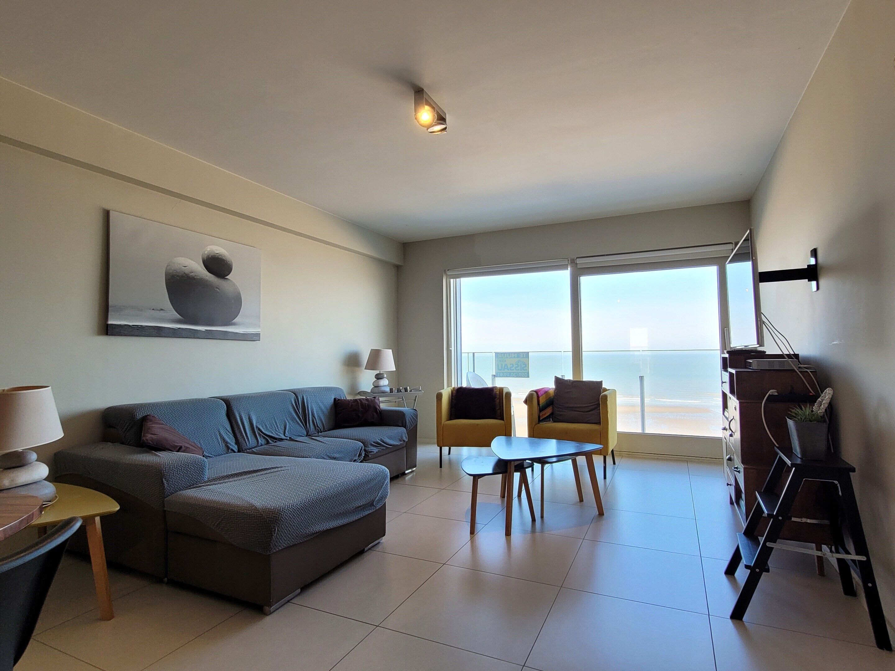 A modern living room with a sofa, two armchairs, a small table, and a TV.