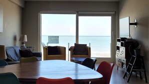 A room with a large table, two chairs, a TV, and a view of the ocean through large windows. - Stylish Holiday Apartment in Middelkerke (Middelkerke)