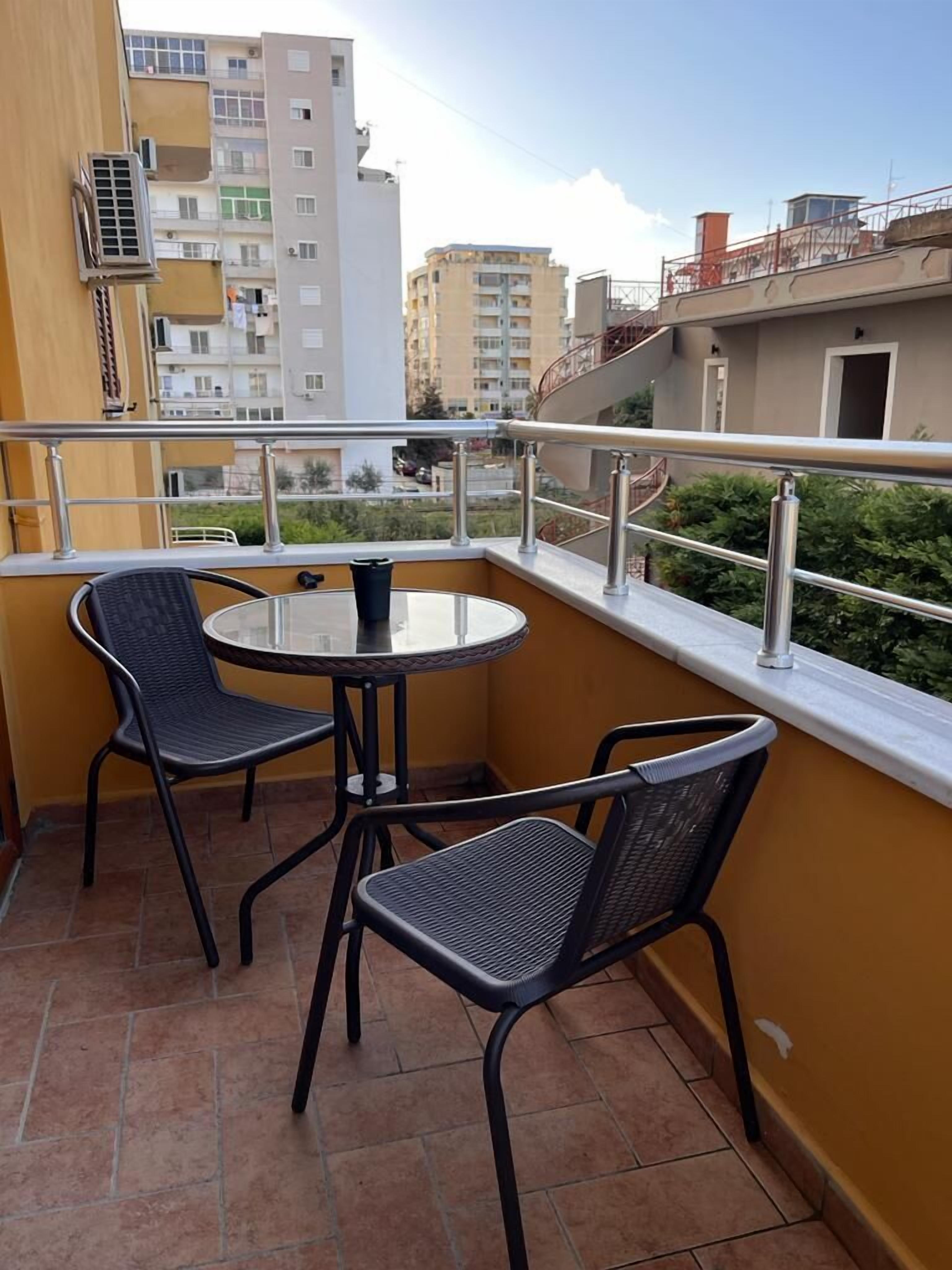 A balcony with two chairs and a table, overlooking a residential area with buildings and greenery.