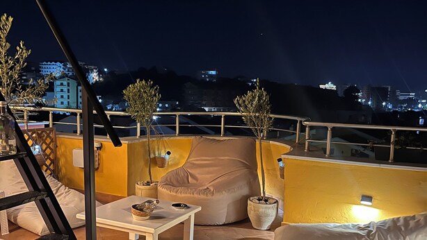 Une terrasse sur le toit avec une table blanche, des coussins de couleur beige et des plantes en pot.