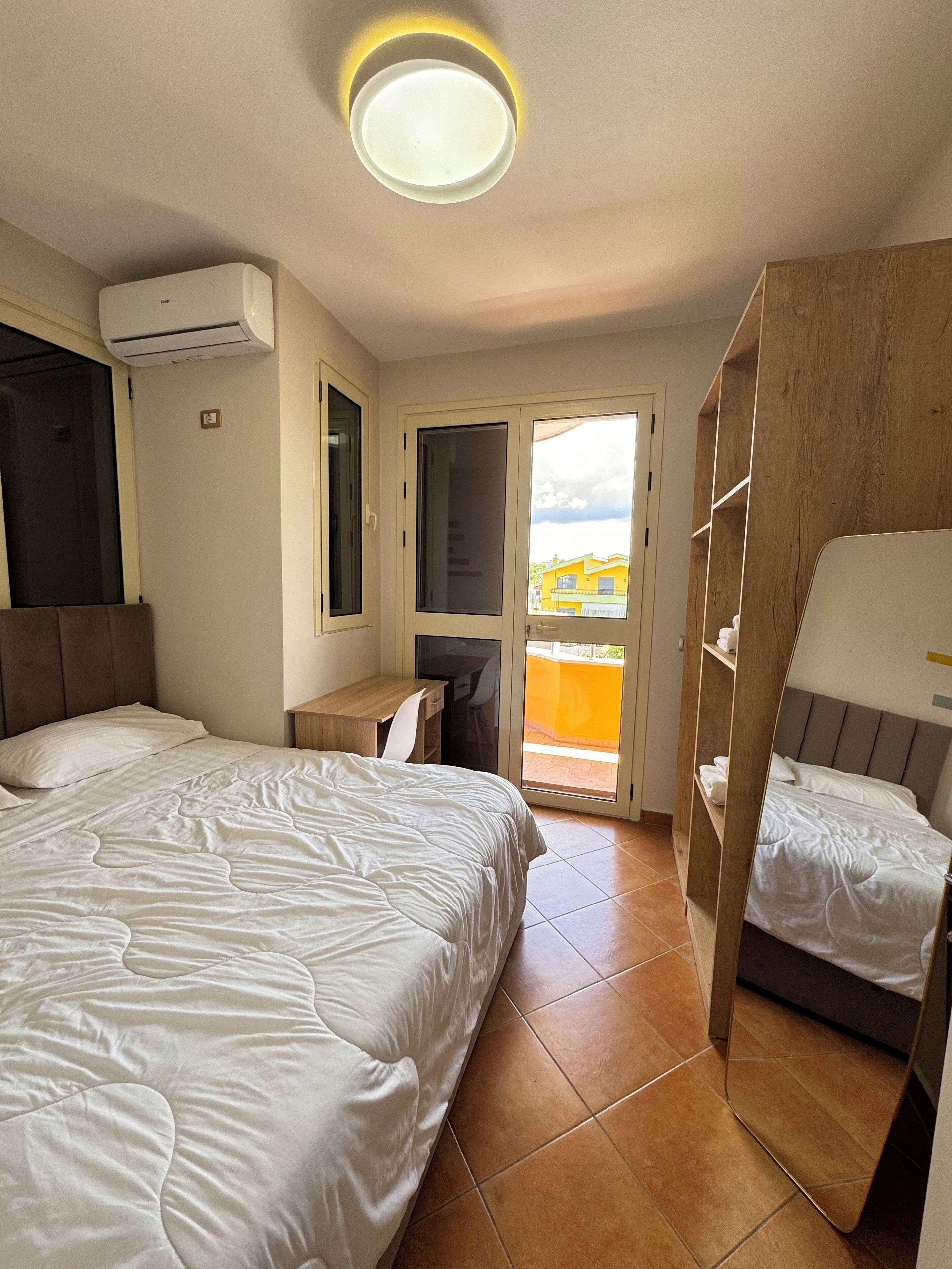 Ein Hotelzimmer mit zwei Betten, einem Schreibtisch, einem Stuhl, einem Kleiderschrank und einem Balkon mit Aussicht.