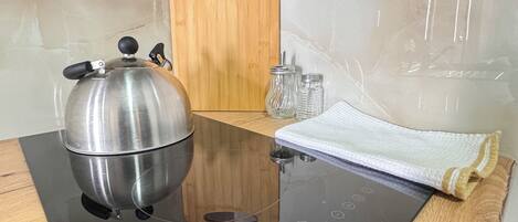 A kitchen with a black induction cooktop, a stainless steel kettle, a wooden cutting board, and a white towel.