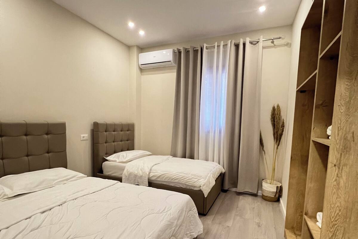 Un dormitori amb dos llits, un armari de fusta i una finestra amb cortines.