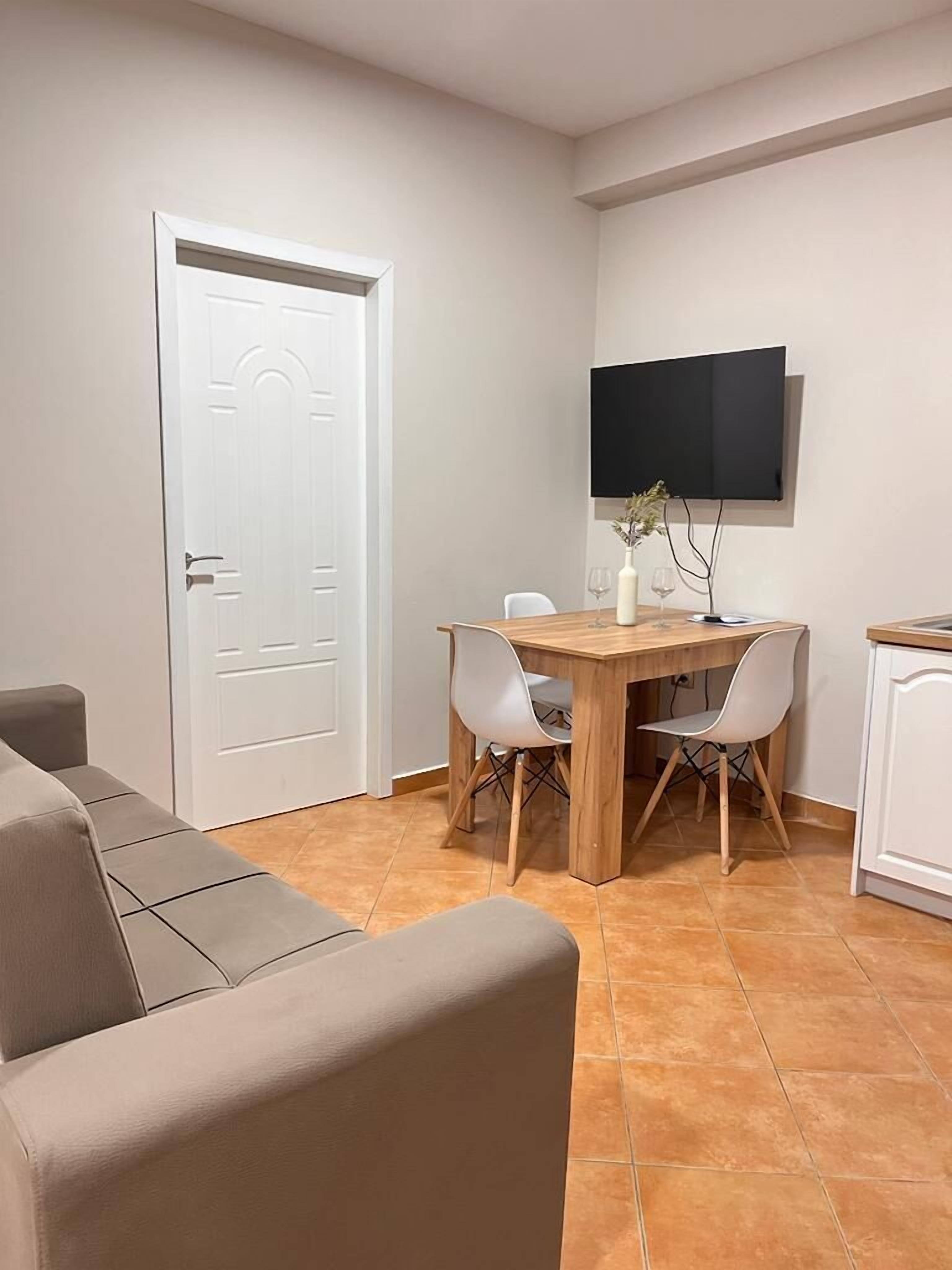 A room with a dining table, two chairs, a TV mounted on the wall, a sofa, and a cabinet.