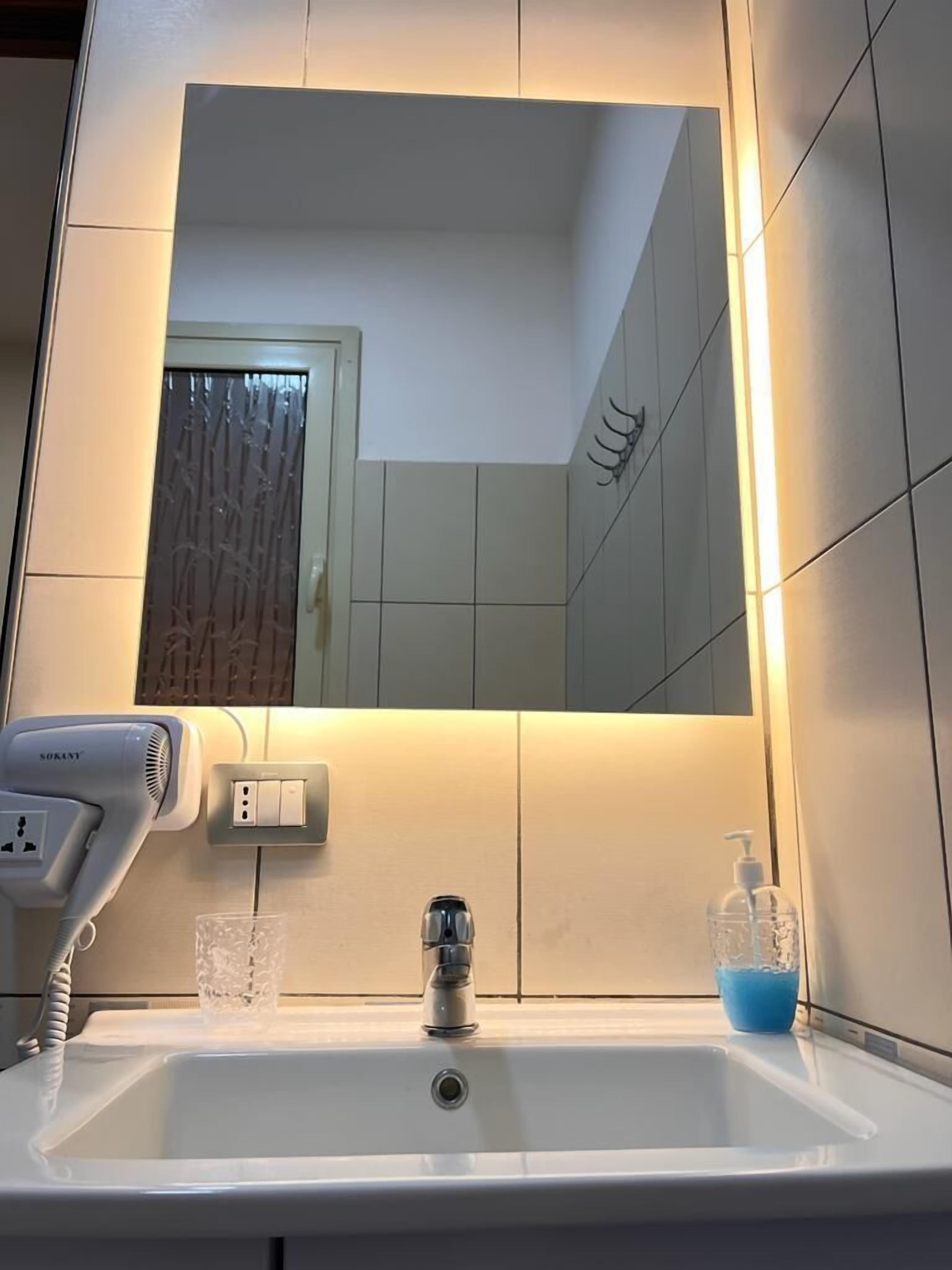 A bathroom with a white sink, a mirror, a hairdryer, and a glass of water.