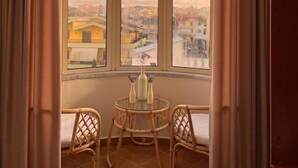 Une pièce dotée d’une grande fenêtre, de deux fauteuils en osier, d’une petite table ronde et d’un luminaire suspendu.