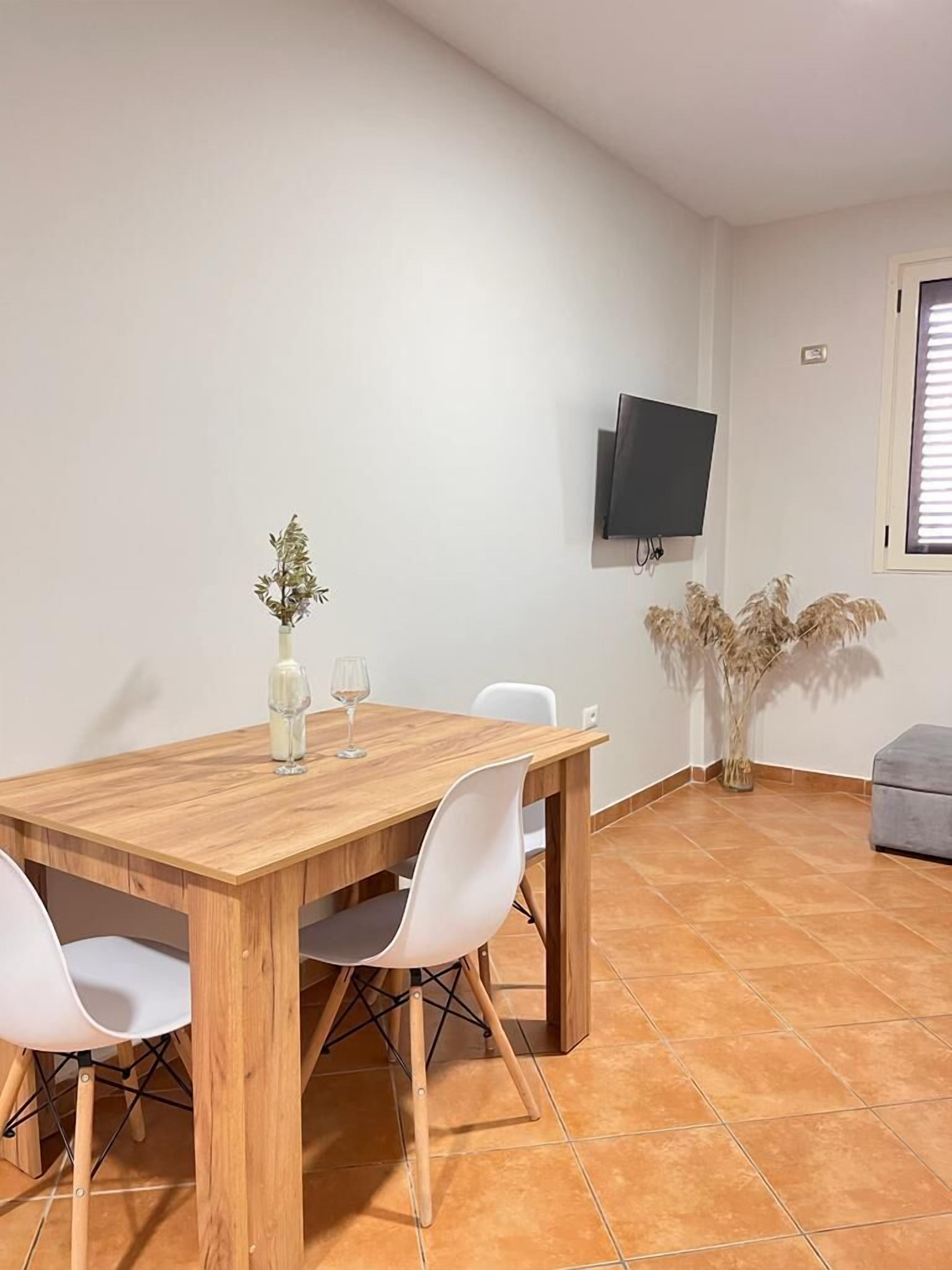 A dining area with a wooden table, white chairs, a vase with flowers, and a television mounted on the wall.