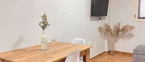 A dining area with a wooden table, white chairs, a vase with flowers, and a television mounted on the wall.