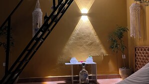 Un escalier avec un luminaire au-dessus, une table avec une bouteille et un bol, et une plante dans le coin.