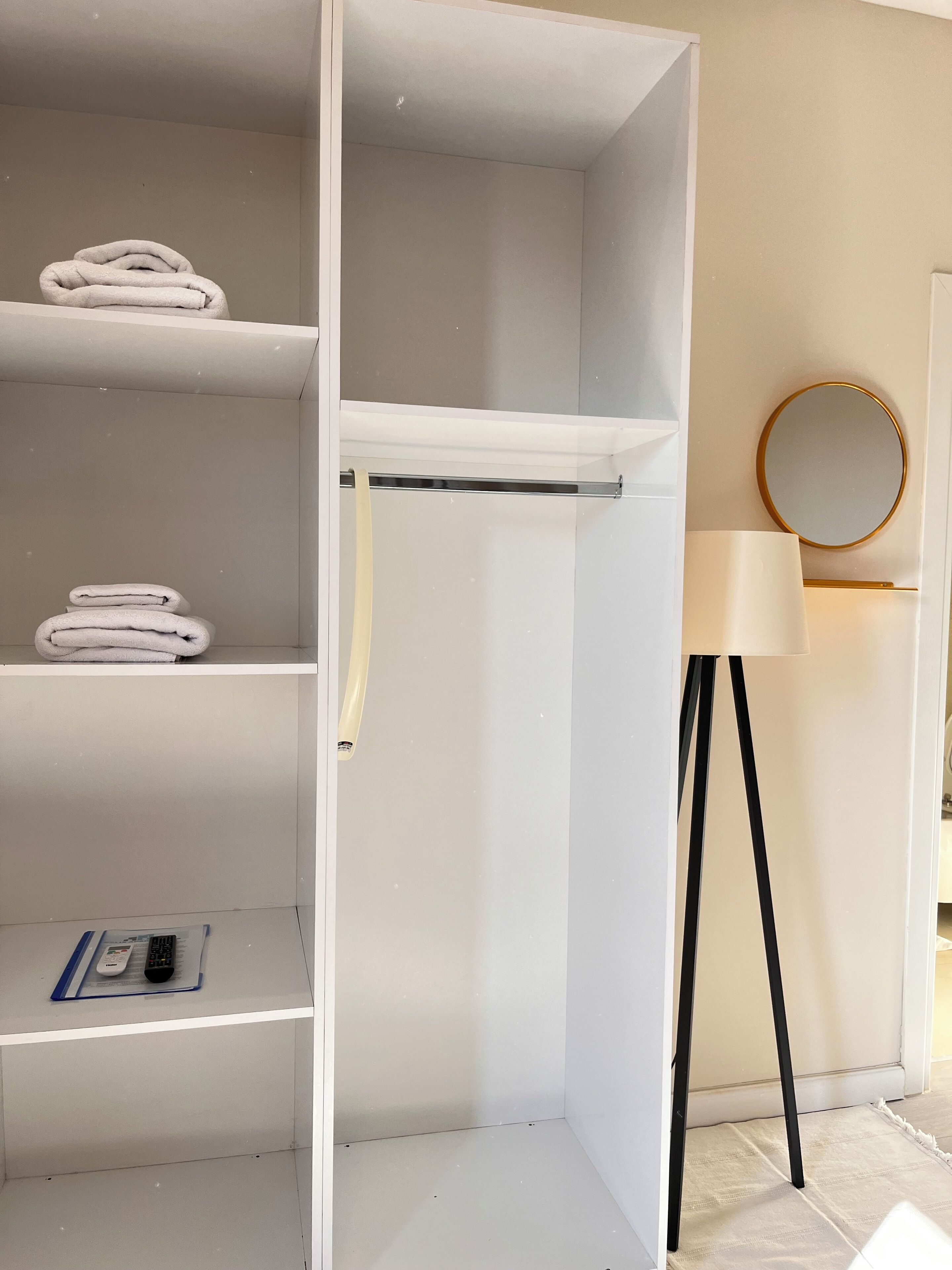 Un armario blanco con varios estantes, una barra para colgar ropa y una mesita con un mando a distancia.