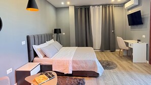 Une chambre d’hôtel moderne équipée d’un lit, d’un bureau, d’une chaise, d’une télévision et d’un luminaire au plafond.