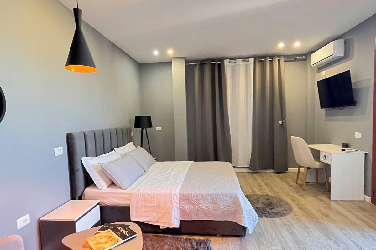 Habitació d'hotel moderna amb un llit, una taula de treball, una cadira, un televisor i una làmpada al sostre.