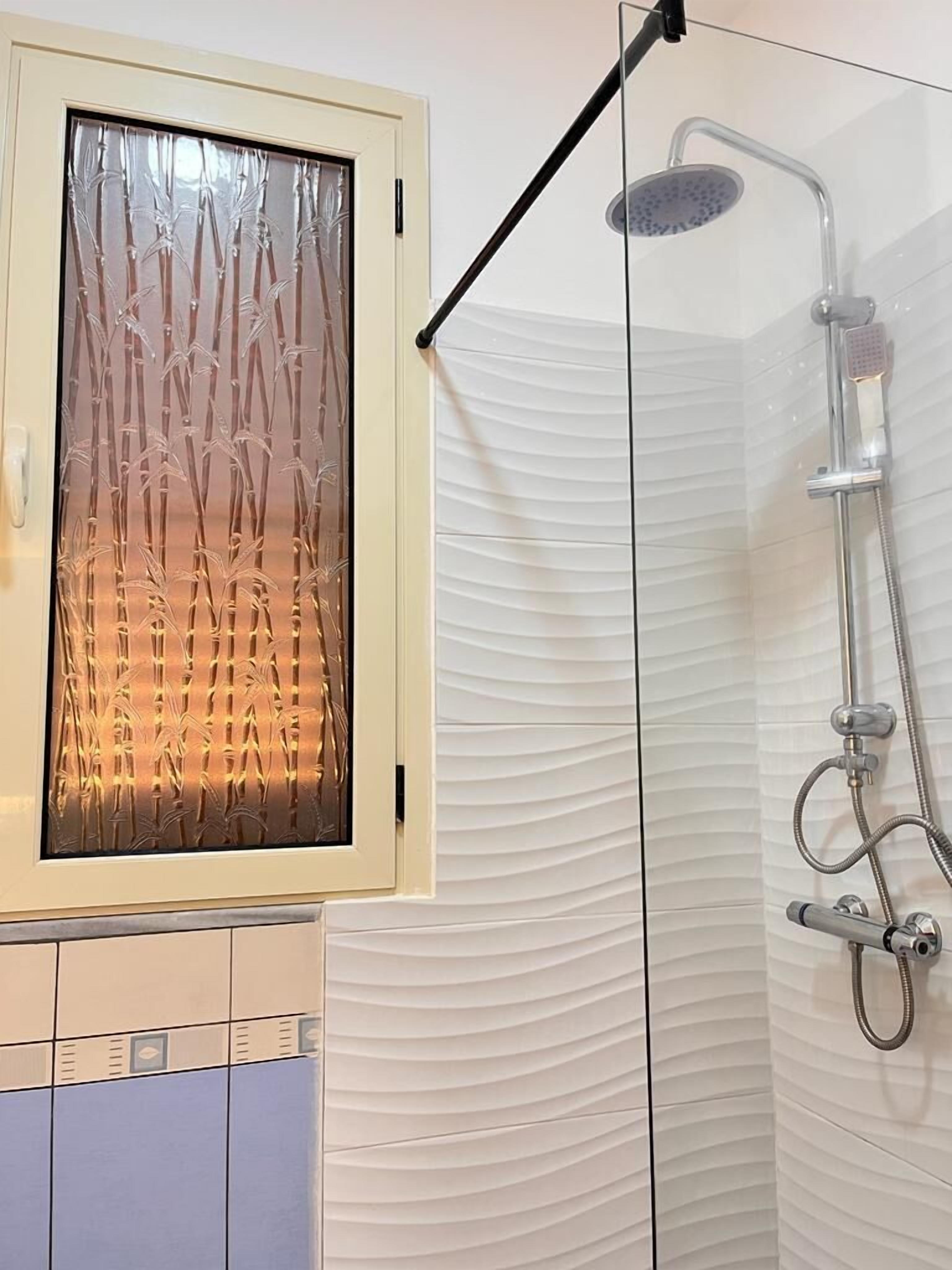 A bathroom with a glass shower enclosure, a white textured wall, and a frosted glass door with bamboo design.