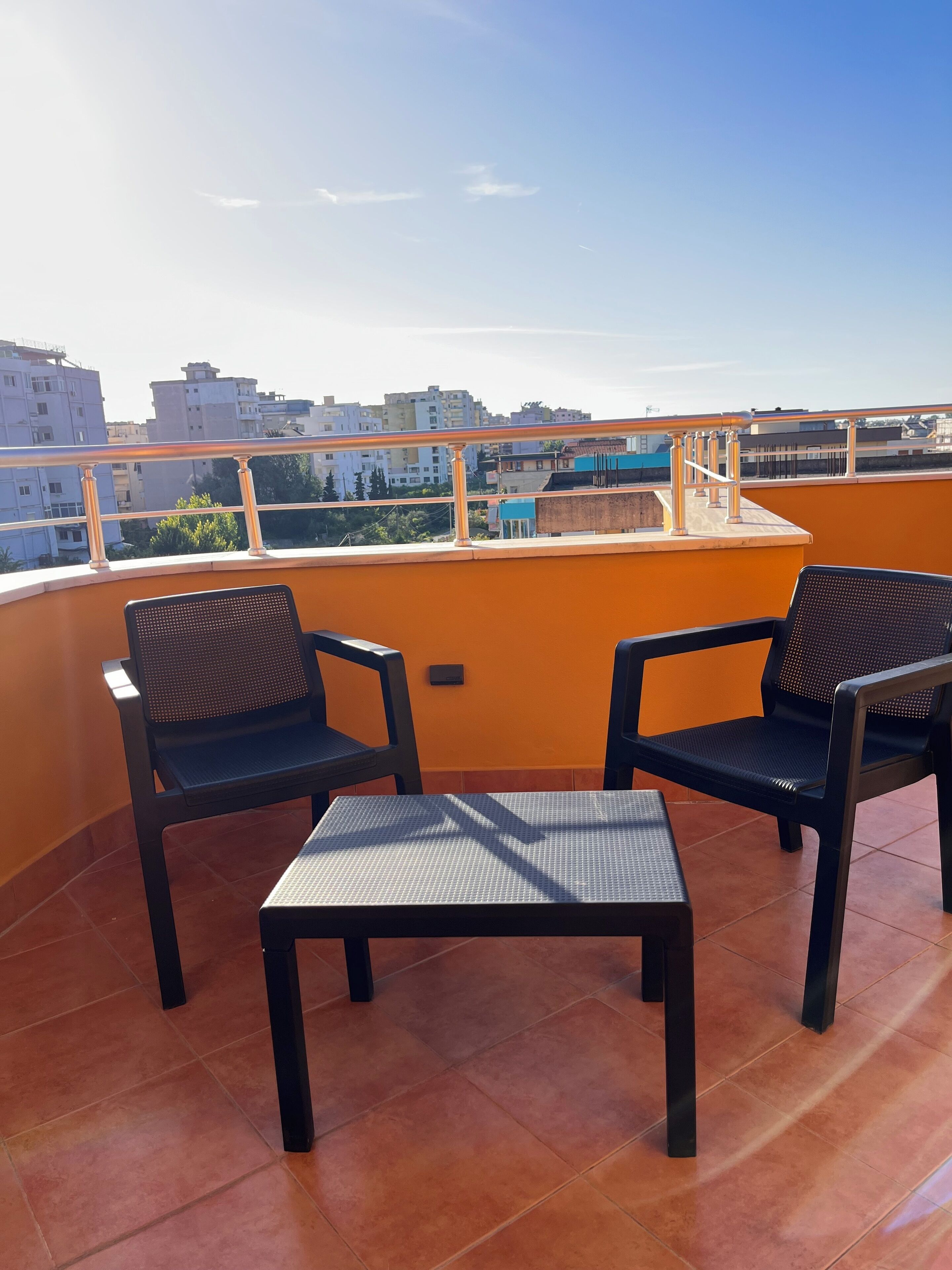 A rooftop terrace with two chairs and a table, overlooking a cityscape.