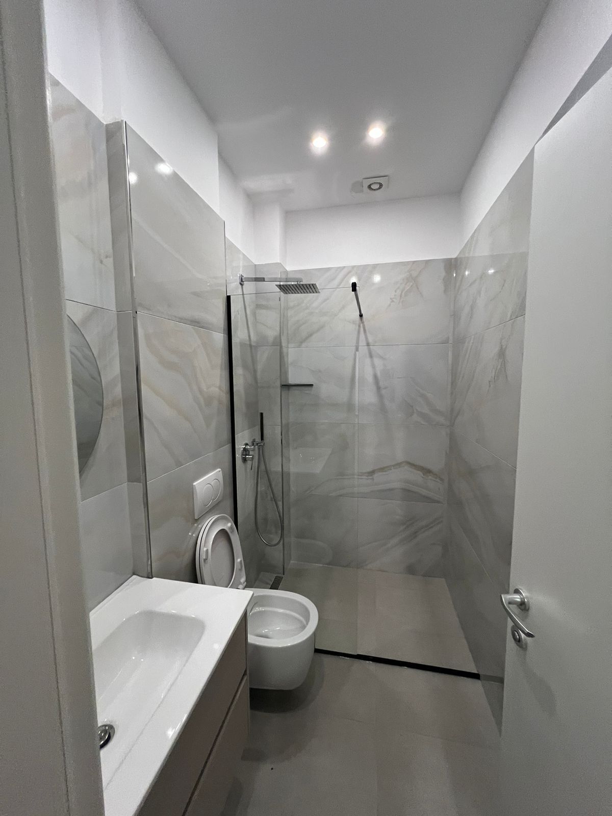 Un bagno moderno con cabina doccia in vetro, un water e un lavandino.