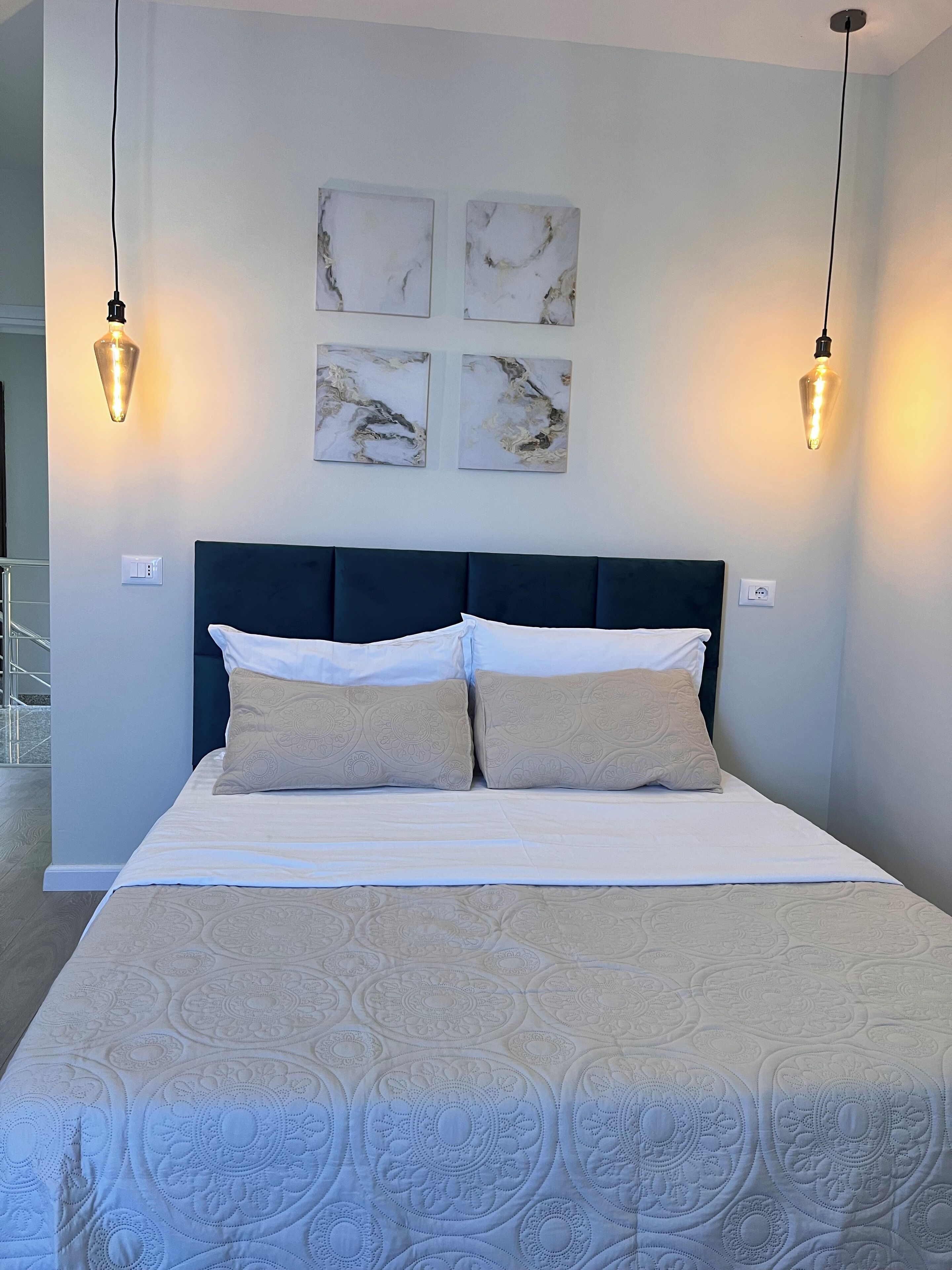 A neatly made bed with a dark headboard, two bedside lamps, and three wall-mounted light fixtures.
