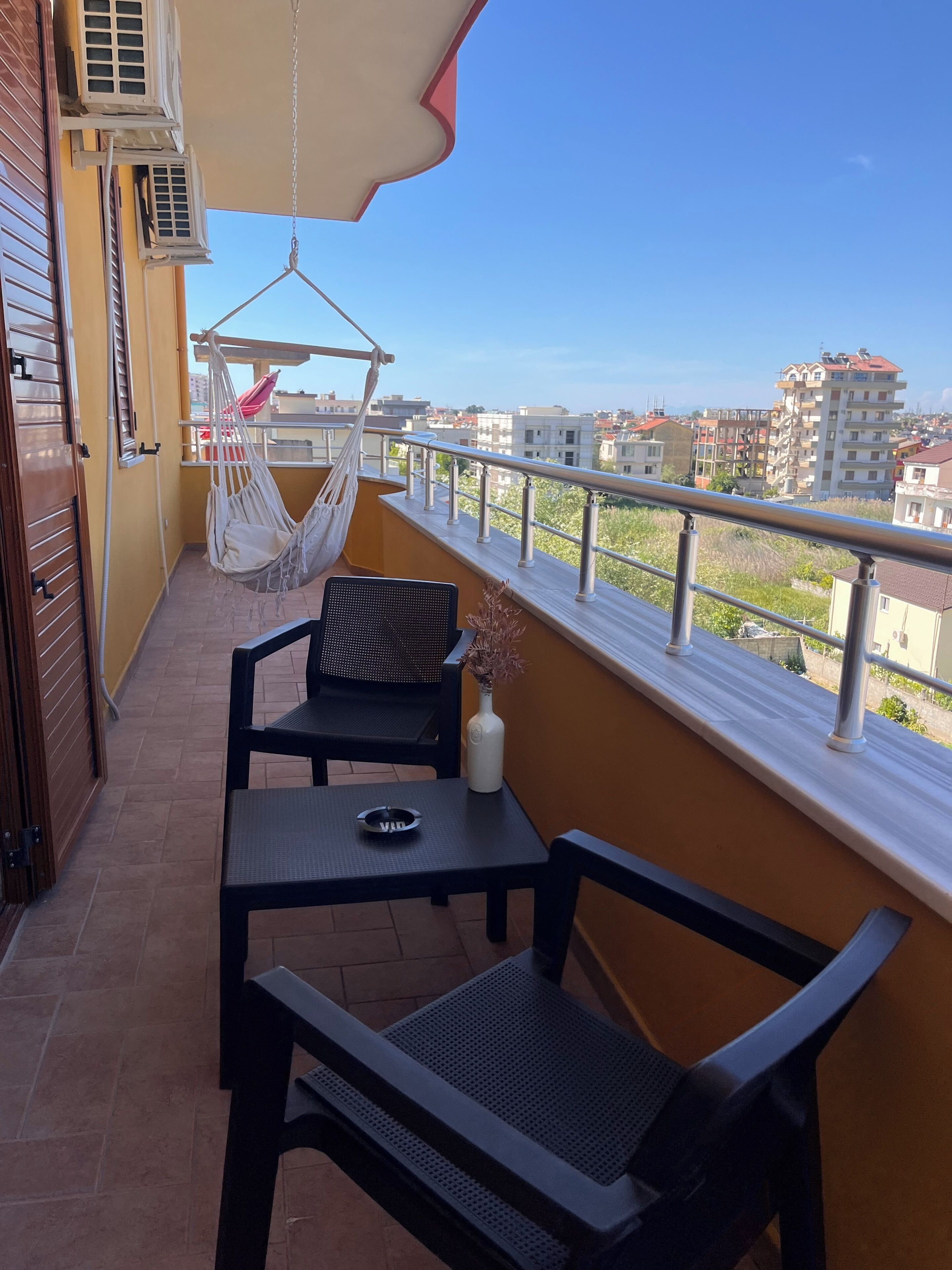 A balcony with a table and chairs, a hanging hammock, and a view of the cityscape.