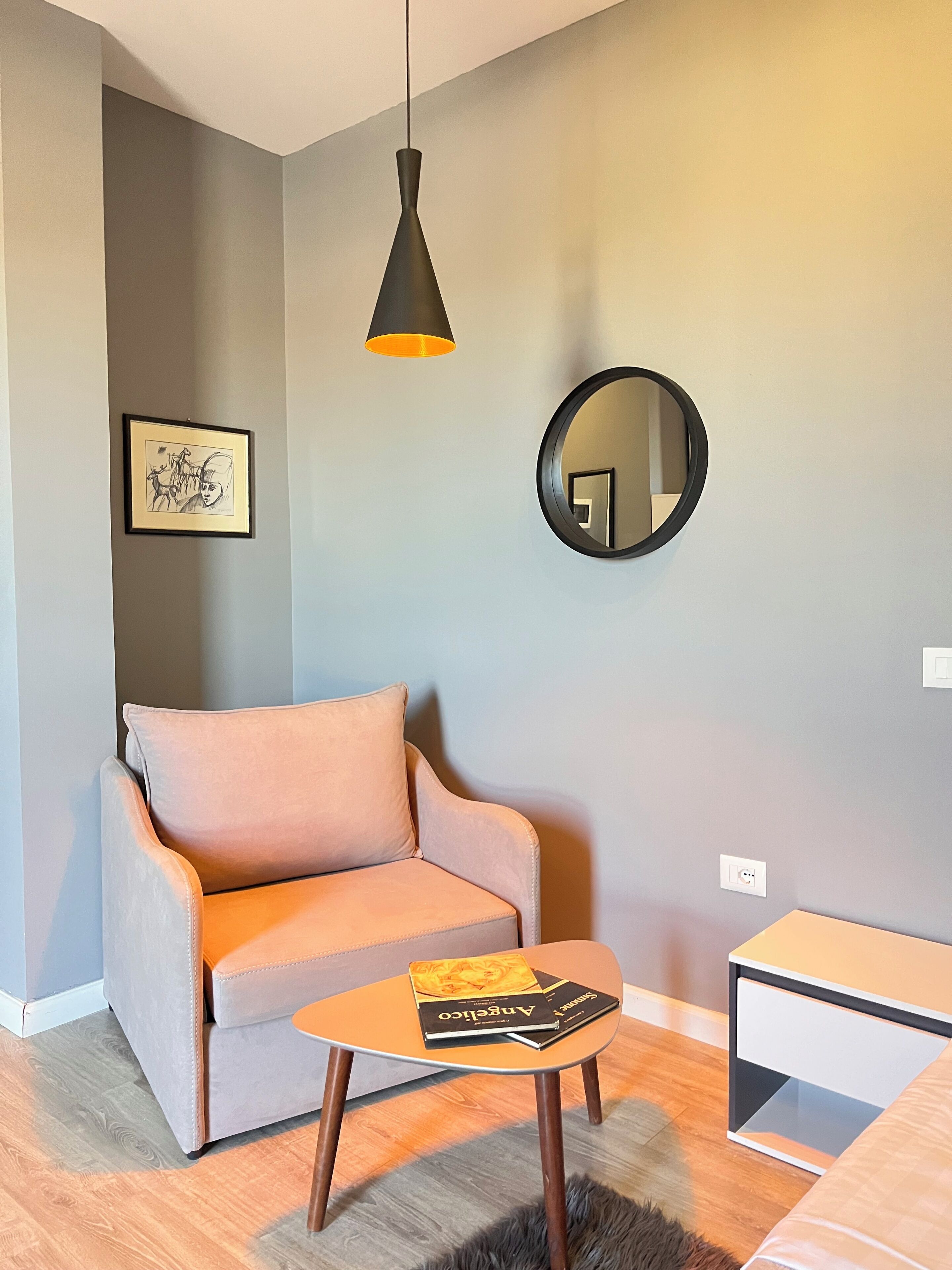 Una sala de estar moderna con un sofá gris, una mesita de centro con libros, un espejo redondo y una lámpara colgante.